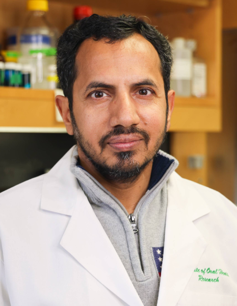 Man with black hair wearing a white coat in a lab setting
